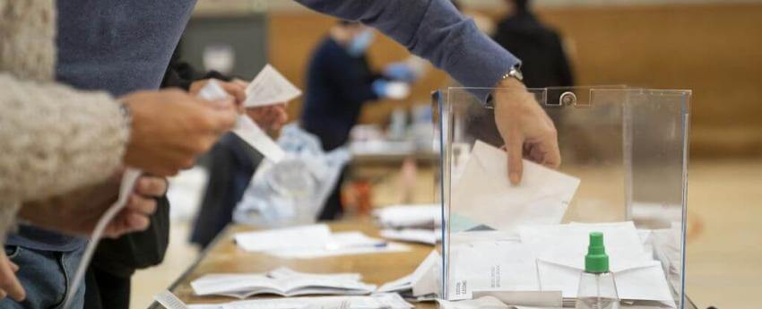 Una urna electoral sobre una taules i unes mans que estan introduint el vot a l'urna