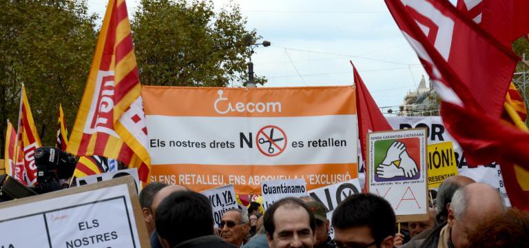 Una pancarta d'ECOM en primer pla enmig d'una manifestació