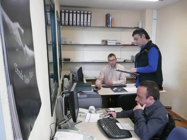 Tres persones en un despatx treballant, una d'elles usuària de cadira de rodes, que està treballant amb l'ordinador