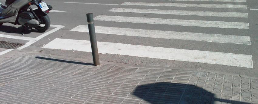 Imatge d'un carrer no accessible. S'hi veu un pas de zebra en l'inici del qual hi ha al mig un pal per evitar que els vehicles es fiquin en la vorera