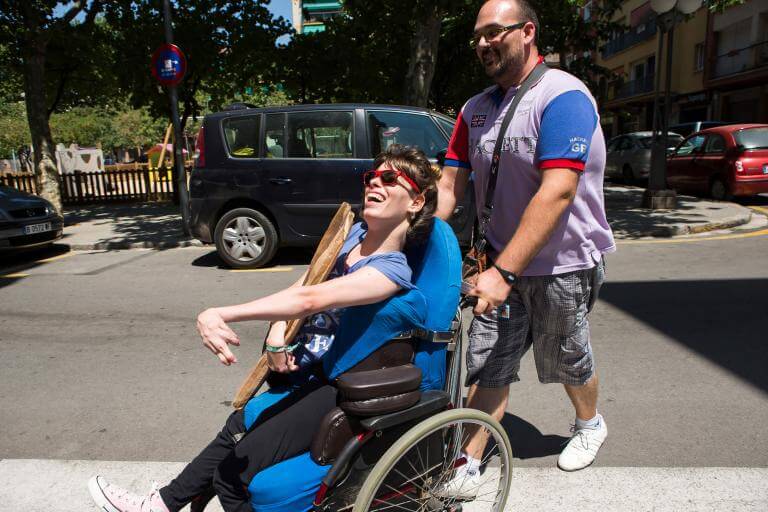 Una noia amb discapacitat física travessant un carrer acompanyada pel seu assistent personal