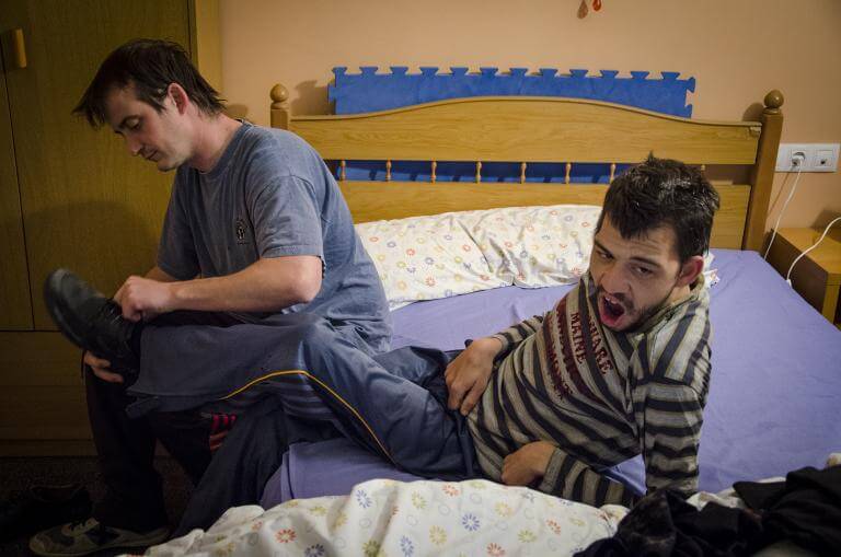 Un noi amb discapacitat estirat en un llit sent atès pel seu assistent personal que l'ajuda a vestir-se