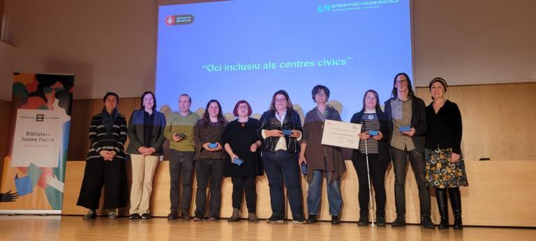 Diverses persones participants en la bona pràctica Centres Cívics Inclusius a l'escenari recollint el reconeixement