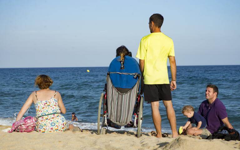 Un assistent personal acompanyant l'usuària que atén en una trobada amb amics a la platja