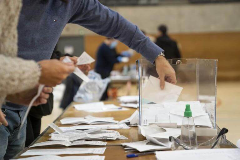 Una urna electoral sobre una taules i unes mans que estan introduint el vot a l'urna