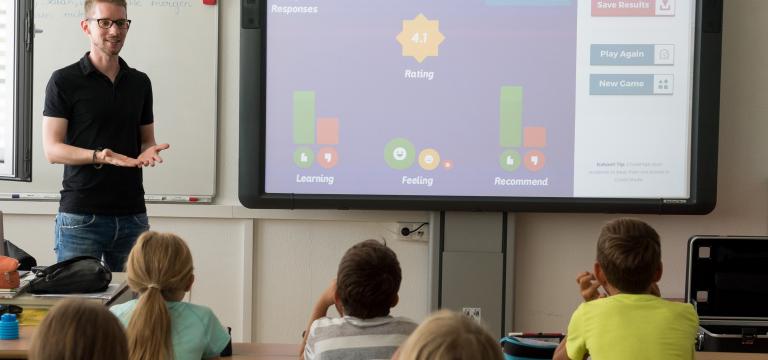 Una aula en què els alumnes atenen el professor i les explicacions que fa al costat de la pissarra