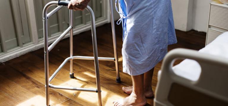Un dona gran dempeus davant el llit ajudant-se d'un caminador