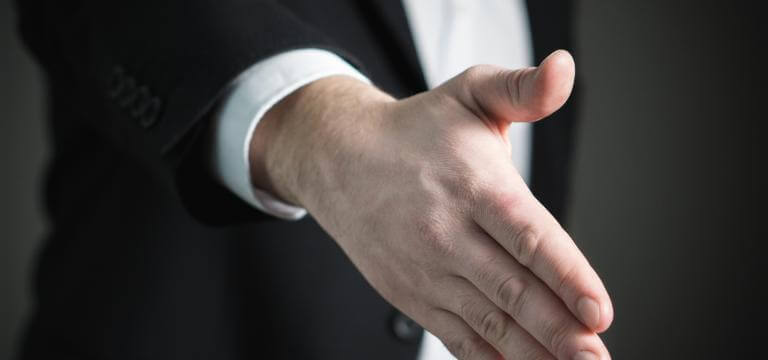 Primer plano de una mano que podría ser de un empresario (va vestido con traje). La mano está en actitud de ofrecer amistad o cerrar un trato