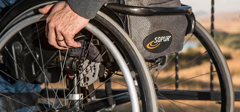 Primer plano de las ruedas de una silla de ruedas; en una de las ruedas se ve la mano de la persona que está sentada en ella