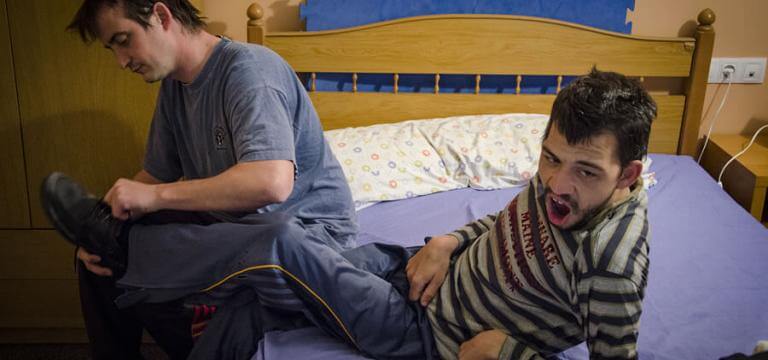 Un home ajudant a un noi a vestir-se al llit estant