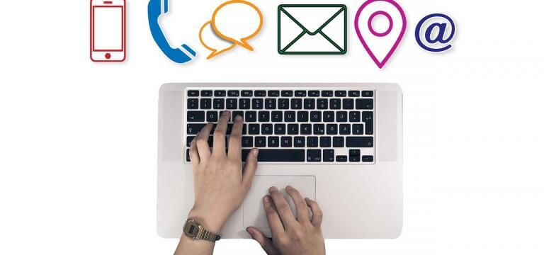 El teclat d'un ordinador amb unes mans treballant-hi i sobre aquesta imatge hi ha diferentes icones: un telèfon fixe, un telèfon mòbil, un sobre (adreça postal), el símbol de la ubicació...
