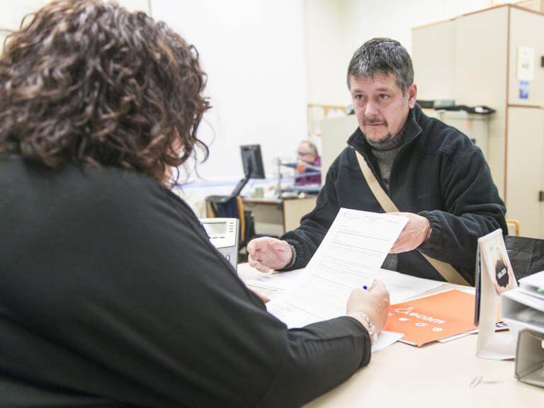 Una tècnica d'ECOM d'esquenes asseguda en una taula atenent a una persona que asseguda al davant d'ella li mostra un paper