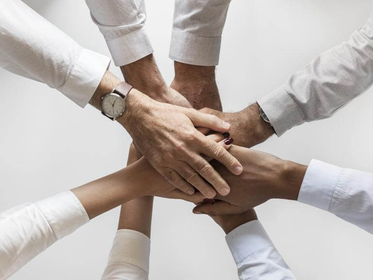 Les mans de diverses personas posades unes a sobre de les altres, com suma d'esforços